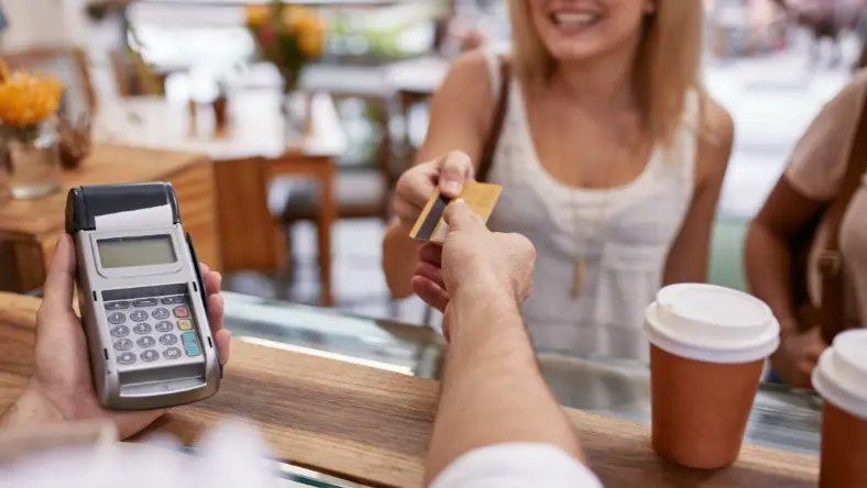 Woman passing credit card to cashier at coffee shop.