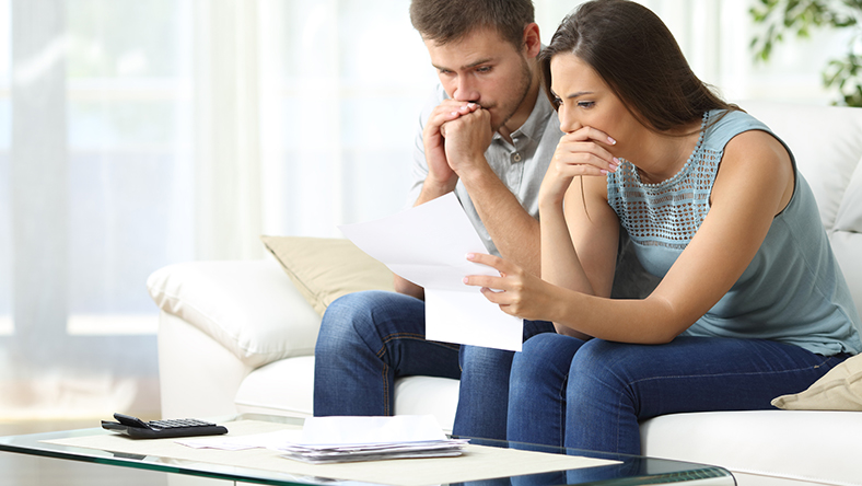A concerned couple reviewing documents sitting on the couch