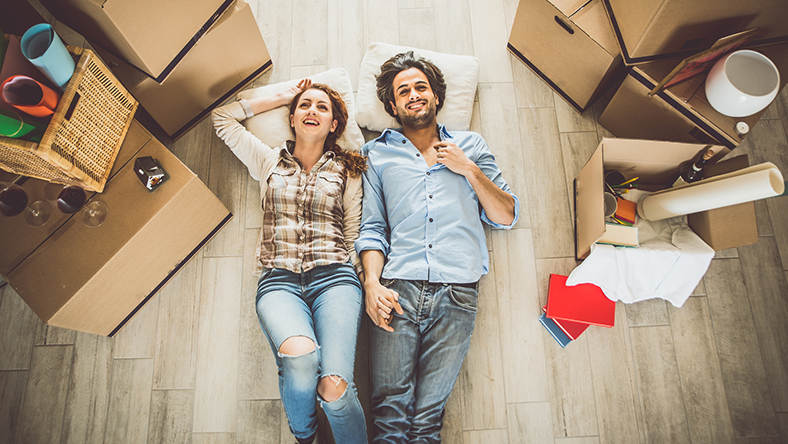 A couple sitting on the floor holding hands surrounding by moving boxes