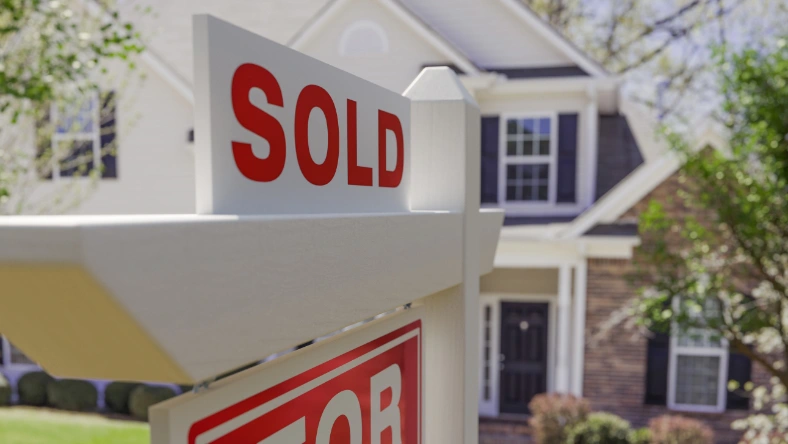 Sold real estate sign in front of a suburban single-family home.
