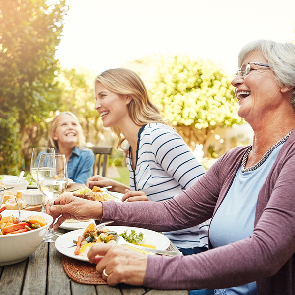 Three generations laughing together at outdoor lunch.